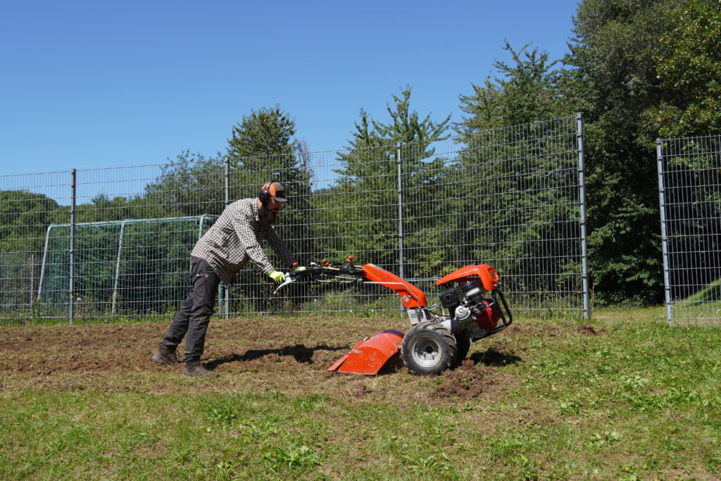 Eine Person bearbeitet den Wiesenboden mit einem Einachser.